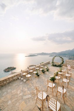 Sveti Stefan adasının yukarısındaki gözlem güvertesindeki yuvarlak düğün kemerinin önünde sandalyeler duruyor. Karadağ. Yüksek kalite fotoğraf