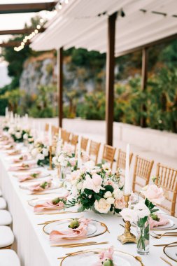 Bahçedeki bir gölgeliğin altında çiçek buketleri ve küçük narlar bulunan şölen masası. Yüksek kalite fotoğraf