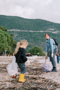 Annem sahilde çöp toplamasına yardım eden küçük bir kıza bakıyor. Yüksek kalite fotoğraf