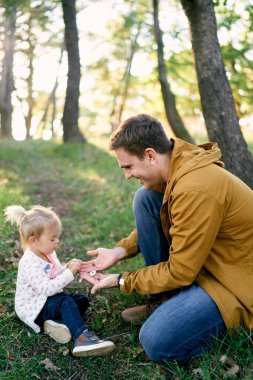 Küçük kız yeşil çimlerde oturan babasının avuçlarından taşları alıyor. Yüksek kalite fotoğraf