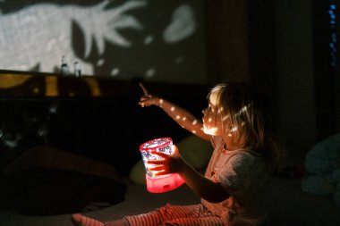 Elinde gece lambası projektörü olan küçük bir kız duvardaki resmi işaret ediyor. Yüksek kalite fotoğraf