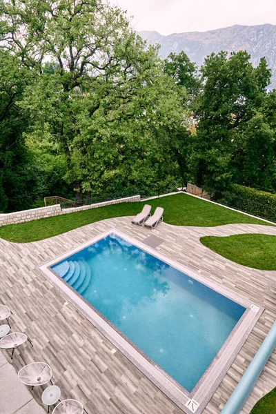 Rectangular pool on a green lawn with sun loungers and chairs near the mansion. Top view. High quality photo