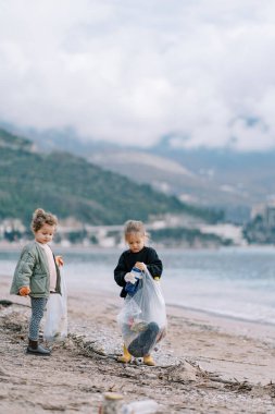 Küçük kızlar kumsalda yürürken çöp poşetlerinde plastik şişe toplarlar. Yüksek kalite fotoğraf