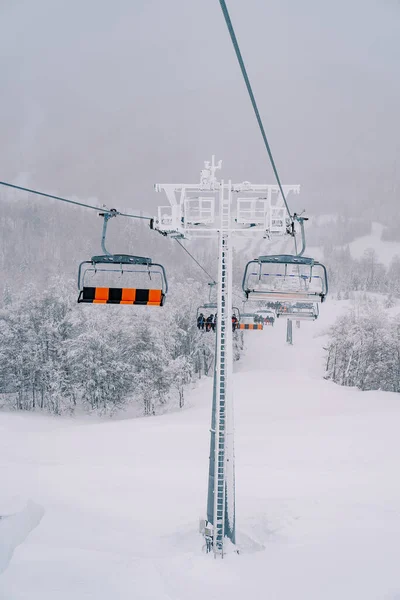 Four-person chairlift seats move along a cable up a snow-covered mountainside. High quality photo