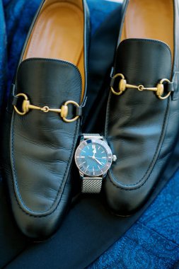 Siyah deri erkek ayakkabıları mavi bir takımda kol saatinin yanında duruyor. Yüksek kalite fotoğraf