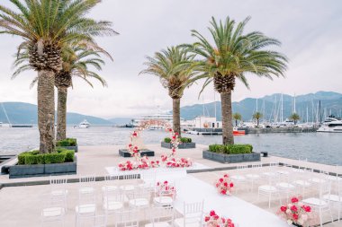 Yuvarlak düğün kemeri, beyaz sandalyelerin önünde demirli yatlarla bir iskelede duruyor. Yüksek kalite fotoğraf