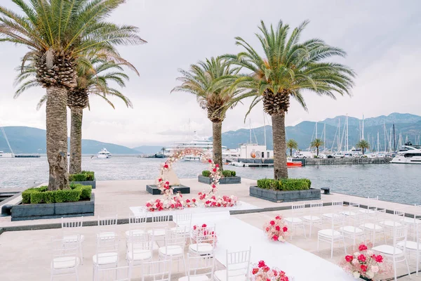 Yuvarlak düğün kemeri, beyaz sandalyelerin önünde demirli yatlarla bir iskelede duruyor. Yüksek kalite fotoğraf