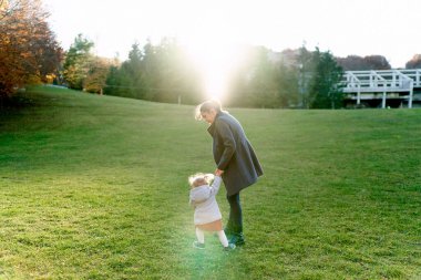 Küçük kız yeşil çimlerin üzerinde annesinin elinden tutar. Arkadan bak. Yüksek kalite fotoğraf