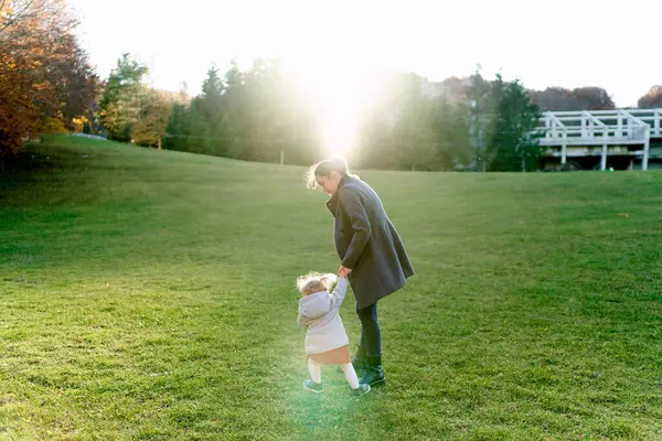 Küçük kız yeşil çimlerin üzerinde annesinin elinden tutar. Arkadan bak. Yüksek kalite fotoğraf
