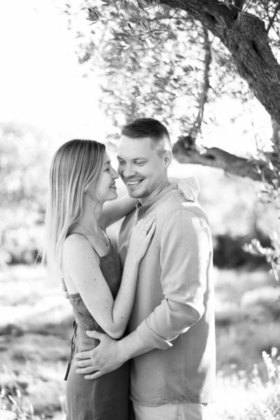 Woman touches her nose to the cheek of smiling man while standing near a tree. Black and white photo. High quality photo
