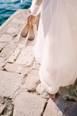 Çıplak ayaklı gelin elinde yüksek topuklu ayakkabılarla kaldırım taşlarının üzerinde duruyor. Kırpılmış. Yüzsüz. Yüksek kalite fotoğraf