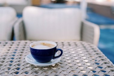 Beyaz bir fincan üzerinde mavi bir fincanda kapuçino bir kafedeki hasır bir masada duruyor. Yüksek kalite fotoğraf