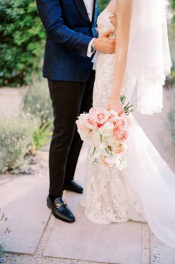 Damat bahçede dikilirken geline bir buketle sarılıyor. Kırpılmış. Yüzsüz. Yüksek kalite fotoğraf