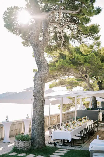 Festive long table stands on the terrace by the sea under sun umbrellas. High quality photo