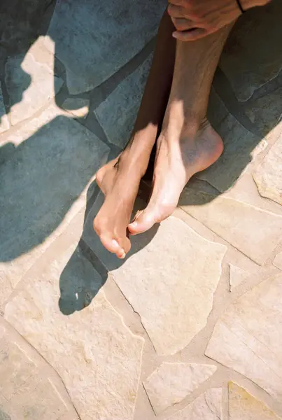 Man leg touches woman leg while sitting on a tile in the sun. Cropped. Faceless. High quality photo