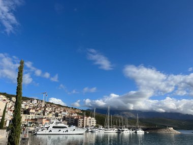 Sailing yachts stand near the shore with colorful houses in Lustica Bay. Montenegro. High quality photo clipart