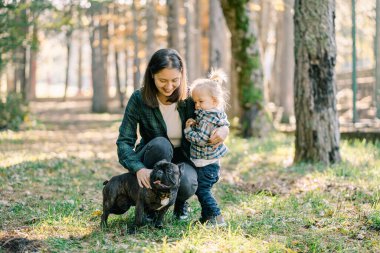 Annem tek eliyle küçük bir kıza sarılıyor, çömelmiş köpeğini ikinci eliyle okşuyor. Yüksek kalite fotoğraf