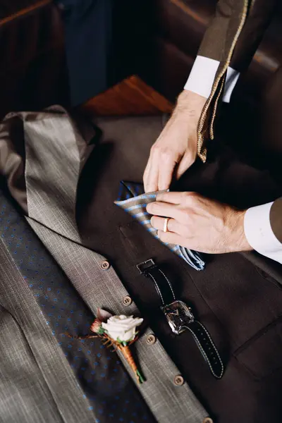 Groomsman folds a handkerchief on groom suit next to the boutonniere. High quality photo