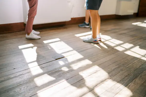 Men in sneakers stand on the wooden floor near the window. Cropped. Faceless. High quality photo
