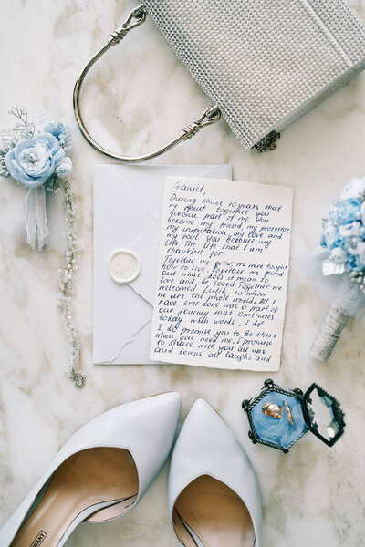 Wedding vow lies on an envelope next to the bride shoes and handbag on a marble table. High quality photo