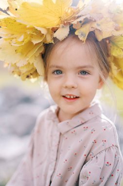 Small mysteriously smiling girl in a wreath of yellow leaves. Portrait. High quality photo clipart
