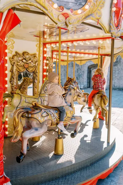 小さな女の子はカラフルなカルーセルに乗って玩具の馬に乗っています バックビュー 高品質の写真 — ストック写真