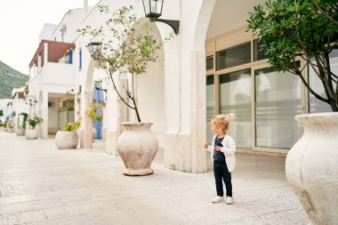 Küçük kız bir apartmanın yanında duruyor ve kafasını çeviriyor. Yüksek kalite fotoğraf