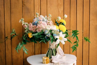 Renkli bir düğün buketi, tahta bir duvara dayanmış beyaz bir sandalyede yüzüklerle bir kutunun yanında duruyor. Yüksek kalite fotoğraf