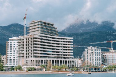 Kule vinçleri, dağların eteğindeki sis içindeki apartmanların inşaat sahasında çalışıyor. Yüksek kalite fotoğraf