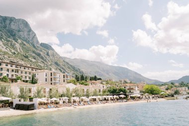 Güneş şemsiyelerinin altındaki güneşlikler Huma Kotor Bay Oteli 'nin özel plajında duruyor. Dobrota, Karadağ. Yüksek kalite fotoğraf