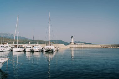 Yelkenli yatlar ve katamaranlar, deniz feneri olan büyük bir dalgakıranın yakınındaki marina iskelesinde duruyorlar. Yüksek kalite fotoğraf