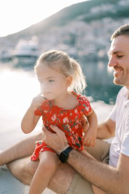 Küçük kız gülümseyen babasının kucağında oturur ve deniz kıyısına bakar. Yüksek kalite fotoğraf