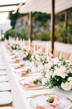Tabaklarda pembe peçeteler ve çiçek buketleri üzerinde küçük nar bulunan uzun festival masası. Yüksek kalite fotoğraf