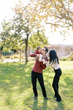 Gülen anne, parkta küçük bir kızı öpen babamın omzuna ellerini koydu. Yüksek kalite fotoğraf