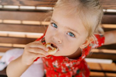 Tahta bir bankta otururken çıtır çıtır simit yiyen küçük bir kız. Yüksek kalite fotoğraf