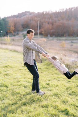 Gülümseyen baba, güneşli bir sonbahar çayırında küçük kızı ellerinden tutar. Yüksek kalite fotoğraf