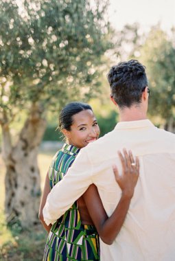 Gülümseyen kadın yeşil bahçedeki adama sarılıp etrafa bakıyor. Arkadan bak. Yüksek kalite fotoğraf