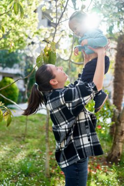 Annem yeşil bir bahçede kollarına gülen küçük bir kız atar. Yüksek kalite fotoğraf