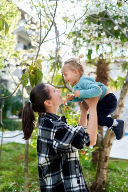 Gülümseyen anne bahçede dururken gülüşen küçük kızı kollarına atar. Yüksek kalite fotoğraf