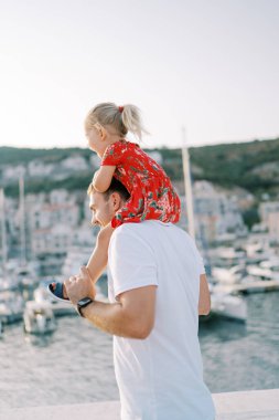 Gülümseyen baba, omuzlarında gülen küçük bir kızla deniz kıyısında duruyor. Yan görüş. Yüksek kalite fotoğraf
