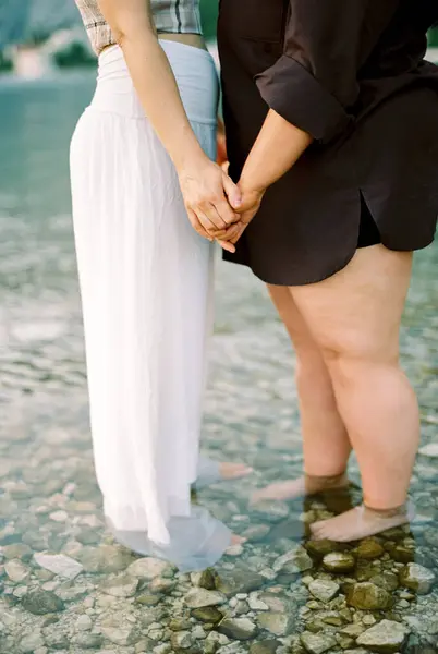 stock image Two women stand barefoot on the rocky bottom of the sea holding hands. Cropped. Faceless. High quality photo