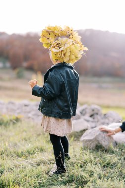Küçük kız sarı yapraklı bir çelenk giyerek çimlerin üzerinde duruyor. Arkadan bak. Yüksek kalite fotoğraf