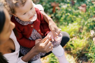 Annem parkta dizlerinin üzerinde oturan küçük bir kızın ellerine dokunuyor. Yüksek kalite fotoğraf