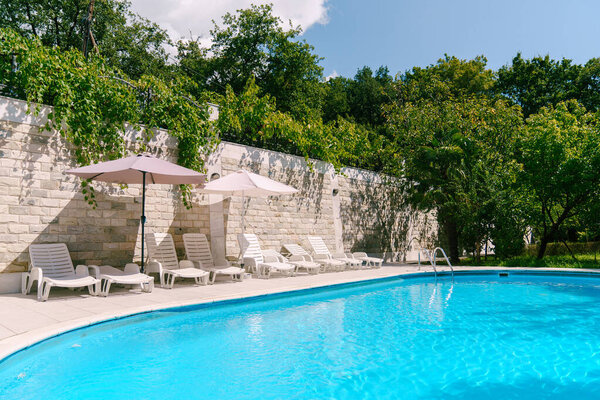 Swimming pool among green trees in the courtyard near a brick fence with sun loungers and sun umbrellas. High quality photo — Stock Image Swimming Pool Green Trees Courtyard Brick Fence Sun Loungers Sun Royalty Free Stock Images