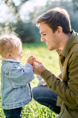 Gülümseyen bir babanın elinde karahindiba üfleyen küçük bir kız. Yüksek kalite fotoğraf