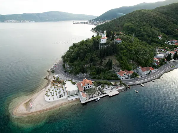 stock image Embankment of a green cape with houses surrounded by forest, a lighthouse and a church on a hill. Lepetane, Montenegro. High quality photo