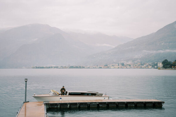 Man moors a motorboat to a wooden pier. Lake Como, Italy. High quality photo