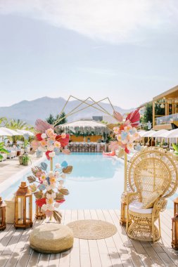 Renkli düğün kemeri hasır bir sandalyenin ve havuz kenarında ahşap mum lambalarının yanında duruyor. Yüksek kalite fotoğraf