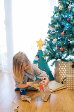 Küçük kız Noel ağacının yanında otururken bir kutudan hediye paketini açıyor. Yüksek kalite fotoğraf