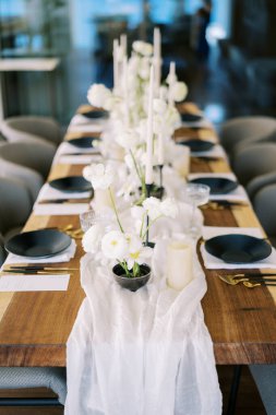 Beyaz çiçek buketleri siyah çanak çömlekli şenlik masasında dar bir masa örtüsünün üzerinde duruyor. Yüksek kalite fotoğraf